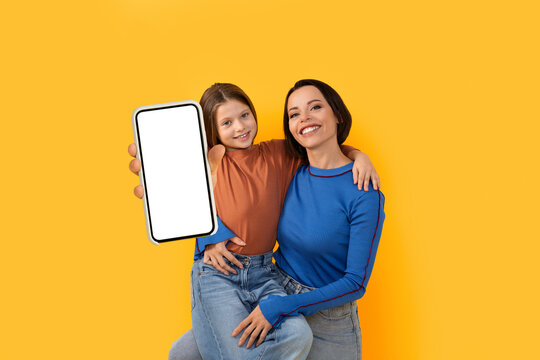 Wall Mural - Smiling Young Mother And Little Daughter Demonstrating Smartphone With Blank White Screen