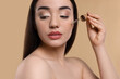 © New Africa - Young woman applying essential oil onto face on beige background
