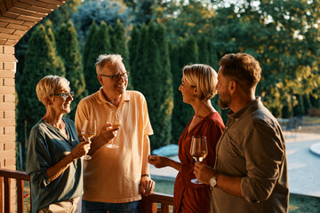 Wall Mural - Happy couple enjoying in wine and conversation with their senior parents on patio at sunset.