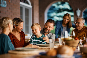 Wall Mural - Happy kid enjoys with his extended family at dining table on patio.