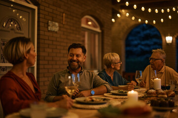 Wall Mural - Happy man drinks wine during family dinner at dining table on patio.