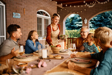 Wall Mural - Happy woman serving salad during family lunch on patio.