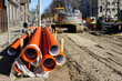 Street reconstruction site, stacked plastic sewage pipes, vertical well, excavator, dewatering pump