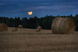 Fototapeta  - Full moon over forest field with bales of straw