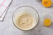 Glass bowl with egg-butter mixture, freshly squeezed orange juice on a gray background. Cooking greek easter  cookies koulourakia step by step instruction. Do it yourself. Step 3. Add orange juice