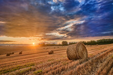 Stubble In A Field With Bales Under A Spectacular Sky With Clouds Through Which The Sun's Rays Shine Through