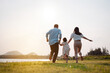 © Kiattisak - Happy family in the park sunset light. family on weekend running together in the meadow with river Parents hold the child hands.health life insurance plan concept.