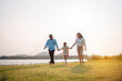 © Kiattisak - Happy family in the park sunset light. family on weekend running together in the meadow with river Parents hold the child hands.health life insurance plan concept.