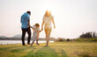 © Kiattisak - Happy family in the park sunset light. family on weekend running together in the meadow with river Parents hold the child hands.health life insurance plan concept.
