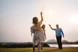 © Kiattisak - Happy family in the park sunset light. family on weekend running together in the meadow with river Parents hold the child hands.health life insurance plan concept.