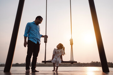 Wall Mural - Happy family enjoying with swing in the park at sunset outdoor in nature, Weekend activity of family life together.