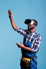 Construction worker wearing virtual reality goggles against blue background. African american builder enjoying 3d entertainment offered by modern technology.