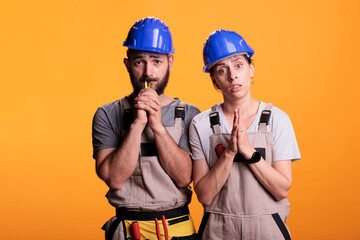 Construction workers doing prayer hands on camera, begging and wishing for luck or fortune. Team of contractors praying, spiritual faithful builders standing over yellow background.