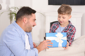 Sticker - Cute little boy presenting his father with gift on sofa at home