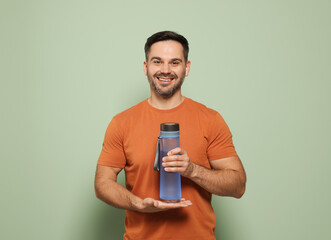 Wall Mural - Happy man holding transparent plastic bottle of water on light green background