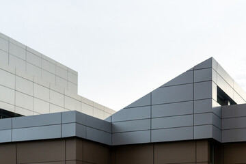 Wall Mural - Commercial external metal composite panels on a building with blue sky and clouds in the background. The durable metal composite panels are two shades of grey in color on the modern building.