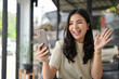 © bongkarn - Smiling Asian woman waving hand, saying hi to her friend during a video call on her smartphone.