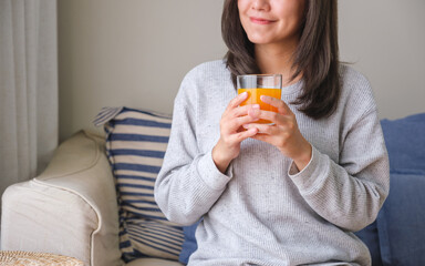 Wall Mural - Closeup image of a young woman holding and drinking fresh orange juice at home