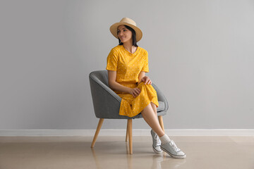 Wall Mural - Beautiful woman sitting in soft armchair near grey wall