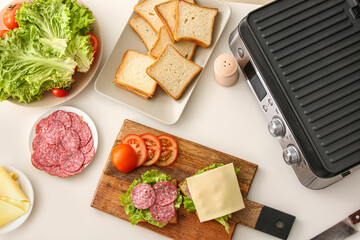 Ingredients for delicious sandwiches and modern electric grill on white table