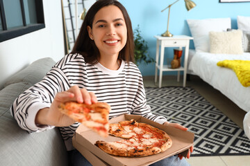 Canvas Print - Young woman with tasty pizza sitting on sofa at home