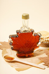 Wall Mural - Bottle and spoon of tasty maple syrup on beige background