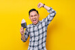 © Bangun Stock Photo - Portrait of excited young Asian man wearing plaid shirt holding a wallet full of cash money in rupiah banknotes in hand and celebrating success isolated on yellow background. people lifestyle concept