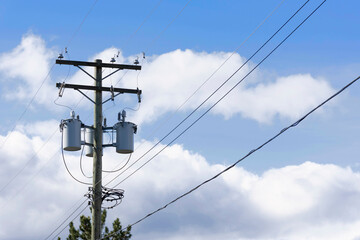 An image of three rural power transformers and power lines on a cloudy day.