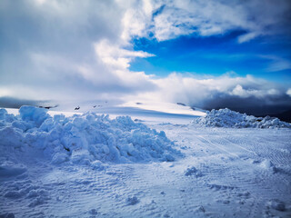 A vast snowy landscape on Langjökull Glacier in Iceland, under a dramatic sky with bright blue patches and billowing clouds