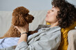 © AnnaStills - Young woman hugging and talking to her dog while lying on sofa in her free time