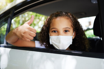 Covid, thumbs up and portrait of a girl in a car for travel, road trip safety and compliance. Free, satisfaction and a little child showing a hand gesture with a face mask for protection in transport