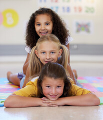 Wall Mural - School kids, lying together and pile on floor, portrait and classroom for smile, solidarity or diversity. Girl, children and class at academy, happy or multicultural friends with support for learning