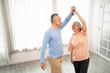 © artitwpd - Romantic and cheerful Asian well-being senior couple enjoy dancing and holding hands to music together with smiles and happiness in the living room. Senior retirement activity at home.