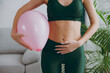 © ViDi Studio - Cropped close up young strong sporty athletic fitness trainer instructor woman wear green tracksuit training hold balloon near belly do exercises at home gym indoor. Workout sport motivation concept.