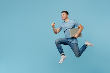 Full body side view young happy IT man wear casual t-shirt jump high run fast hold use work on laptop pc computer isolated on plain pastel light blue cyan background studio portrait Lifestyle concept