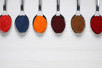 Wall Mural - Spoons with different food coloring on white wooden table, flat lay. Space for text