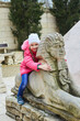 A girl is sitting on a small sculpture of the sphinx.near a replica of the Egyptian pyramid in the miniature park. Travel and tourism.