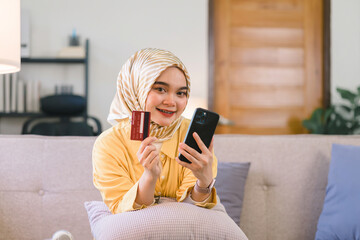 Wall Mural - Portrait of a beautiful Muslim businesswoman wearing a hijab showing a credit card at home.