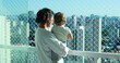 © Marco - Mom holding baby looking at city view from apartment balcony with safety net