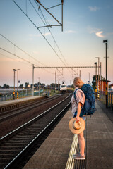 Wall Mural - Woman traveler waiting at train station during sunset. Solo tourist is ready for summer journey