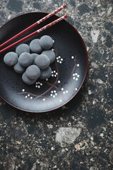 Wall Mural - Black plate with mochi or popular korean snack and dessert, flat lay on a dark-brown granite background, vertical shot, copy space