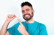 © Jihan - Young man over white background  holding an invisible aligner and pointing at it. Dental healthcare and confidence concept.