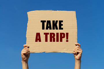 Take a trip text on box paper held by 2 hands with isolated blue sky background. This message board can be used as business concept about travelling.