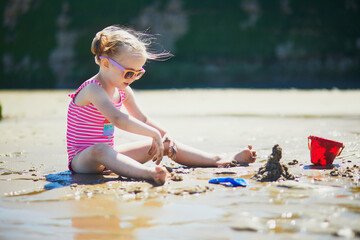 Sticker - Preschooler girl playing on the sand beach at Atlantic coast of Normandy, France