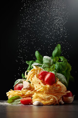 Wall Mural - Homemade raw pasta with tomato, garlic, and basil on a black background.