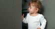 © Marco - One year old baby boy opening kitchen cabinet cupboard closer door. Infant toddler standing at kitchen floor