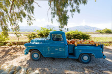 A Vintage Blue Pickup Truck Loaded With Colorful Pumpkins, With Misty Mountains In The Background.