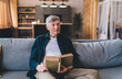 © BullRun - Mature man sitting with book on sofa and looking away