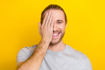 Wall Mural - Portrait of optimistic guy with long hair dressed light t-shirt arm cover eye at ophthalmology checkup isolated on yellow color background