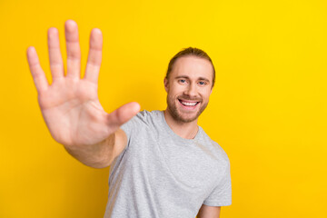 Poster - Photo of toothy beaming pleasant man with long hairstyle wear gray t-shirt showing palm at camera isolated on yellow color background